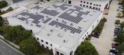 Aerial view of a large commercial building fitted with solar panels on the roof, surrounded by trees and a parking area, showcasing LA Solar Group's commercial services.