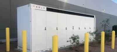 Tesla energy storage system installed outside a commercial building by LA Solar Group, with yellow protective bollards in the foreground.