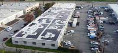 Aerial view of a commercial building with rooftop solar panels, surrounded by parking lots and adjacent buildings, highlighting solar energy installation by LA Solar Group.